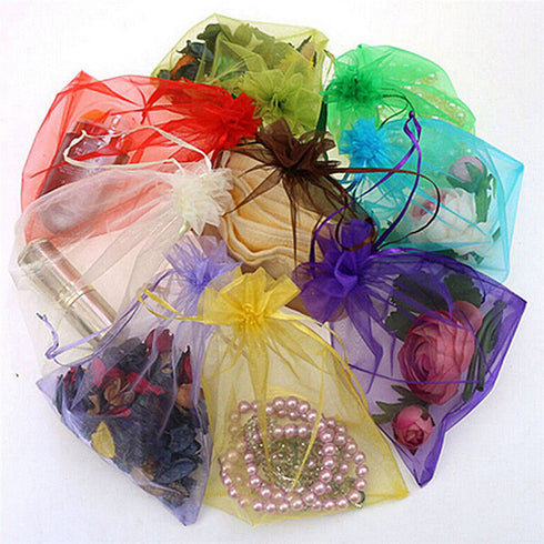 An arrangement of colorful organza gift bags containing assorted treasures like roses, jewelry, and dried flowers, each bag adorned with a WISE OWL 2-Tones Gold Filled Charm Bracelet for Women Fashion Jewelry Chain Gold and Silver on a pristine white background.